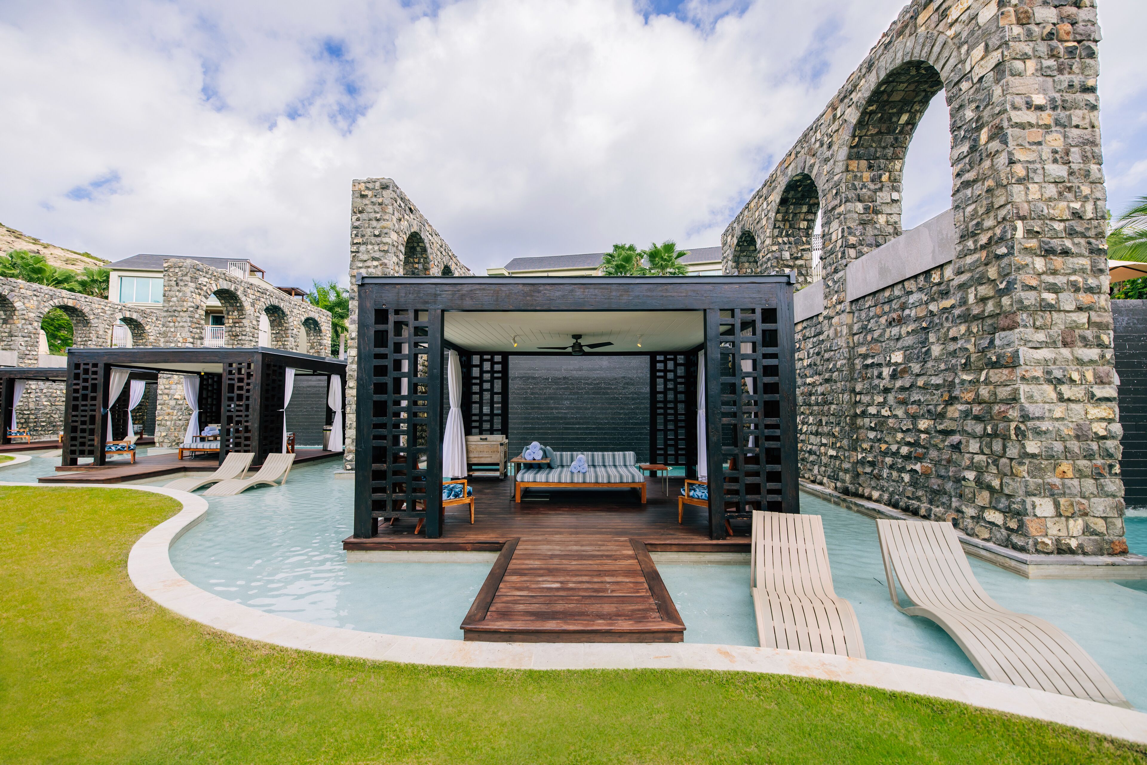 A poolside area with a wooden deck, lounge chairs, and a bed with a canopy.