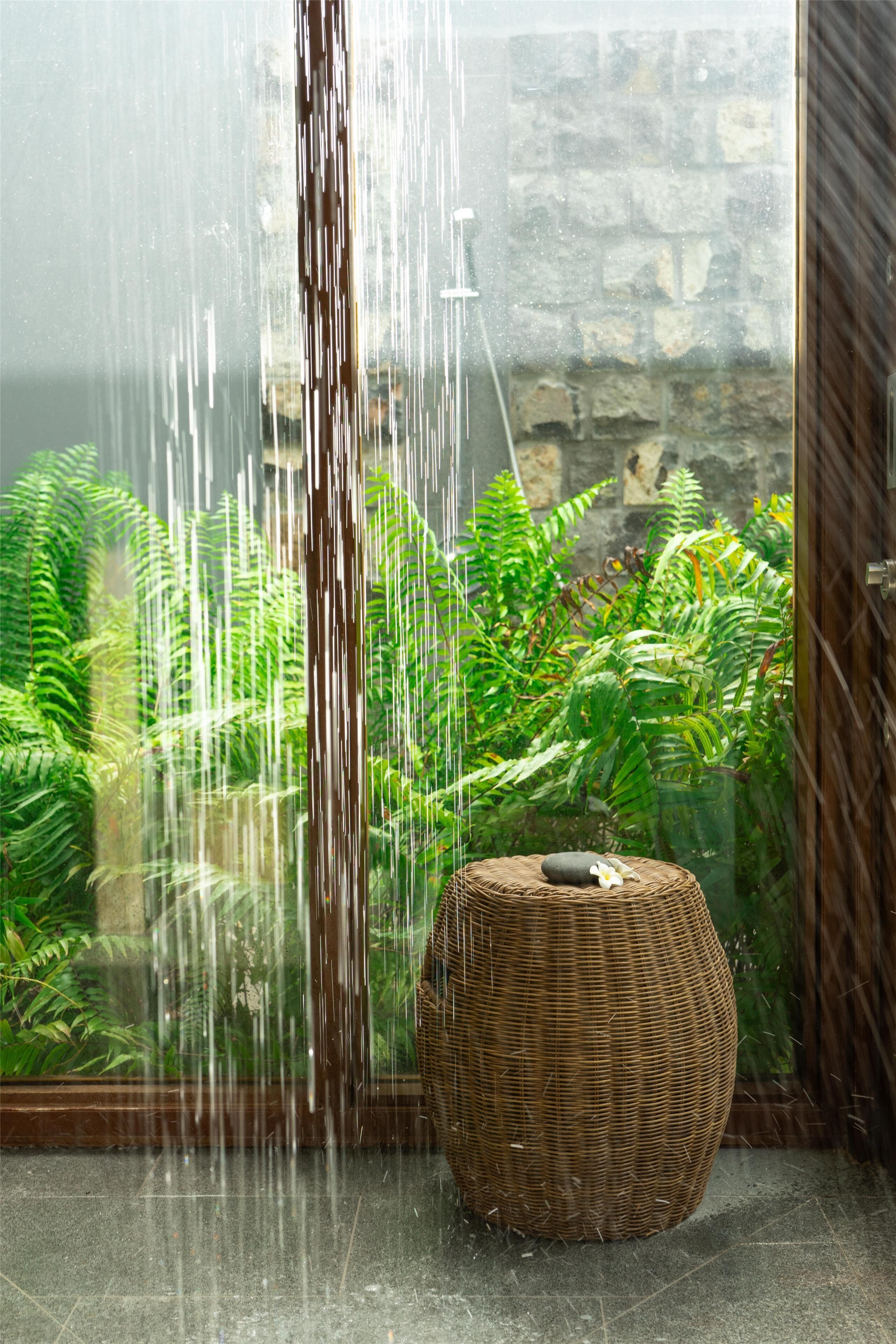 Cabina doccia in vetro con parete in pietra e vegetazione sullo sfondo.