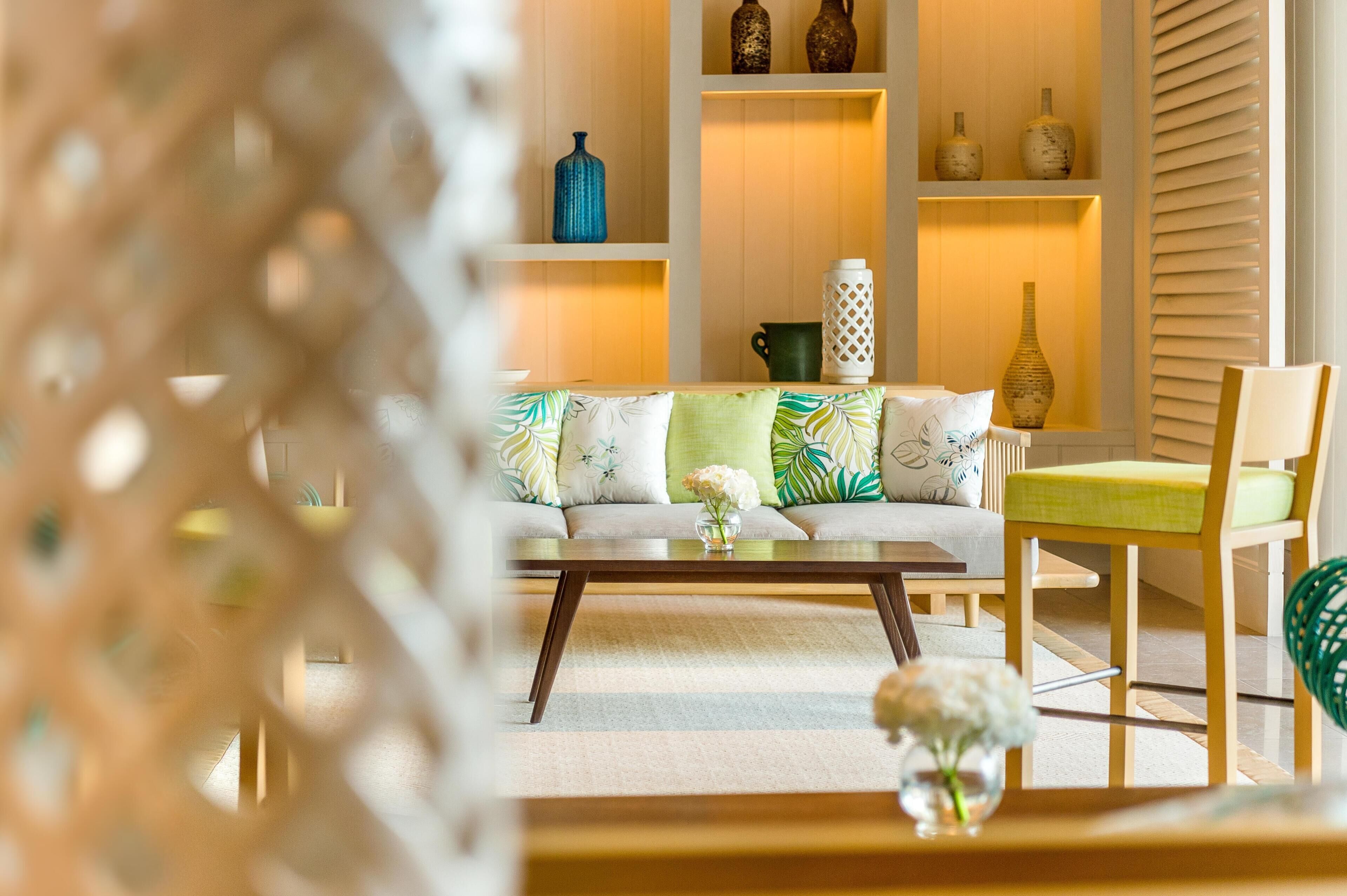 A living room with a sofa, a coffee table, and a chair. There are shelves with decorative items.