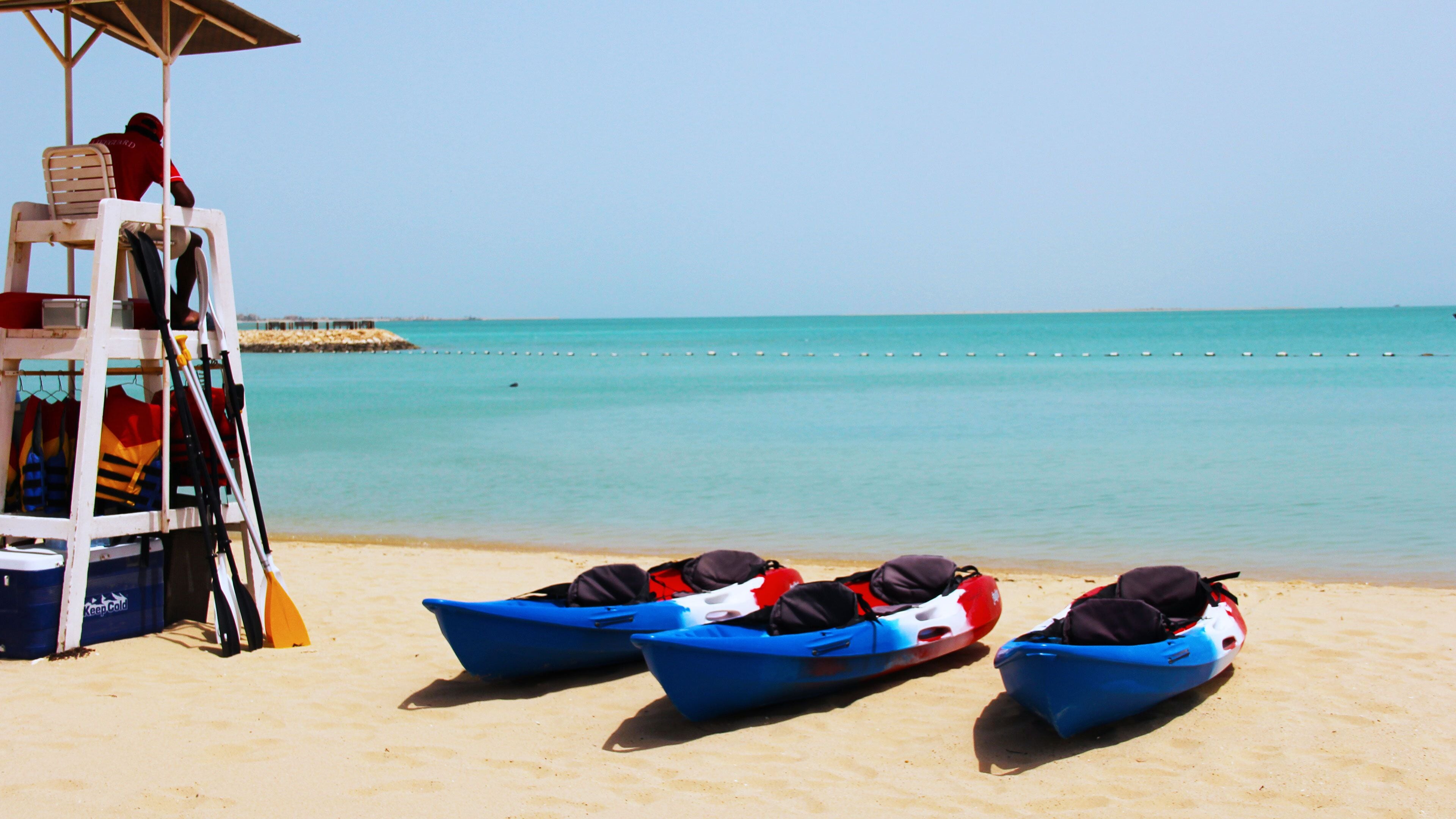 A lifeguard tower with a chair and a row of blue boats on a sandy beach.