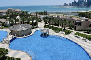 A large swimming pool with a gazebo, palm trees, and a view of the city skyline and beach. - Intercontinental Doha Residences by IHG (Doha)