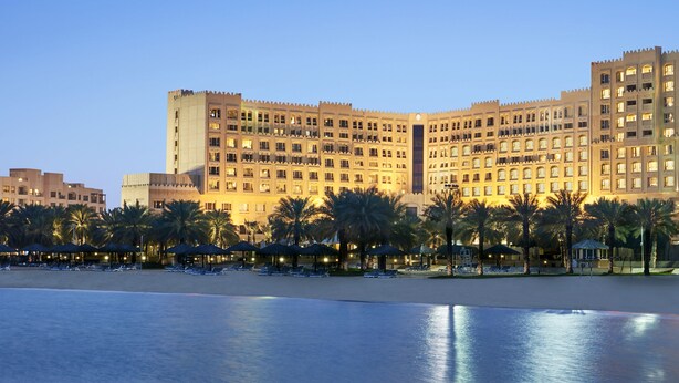 A large hotel with multiple floors and balconies, a beach in the foreground, and palm trees. - Intercontinental Doha Residences by IHG (Doha)