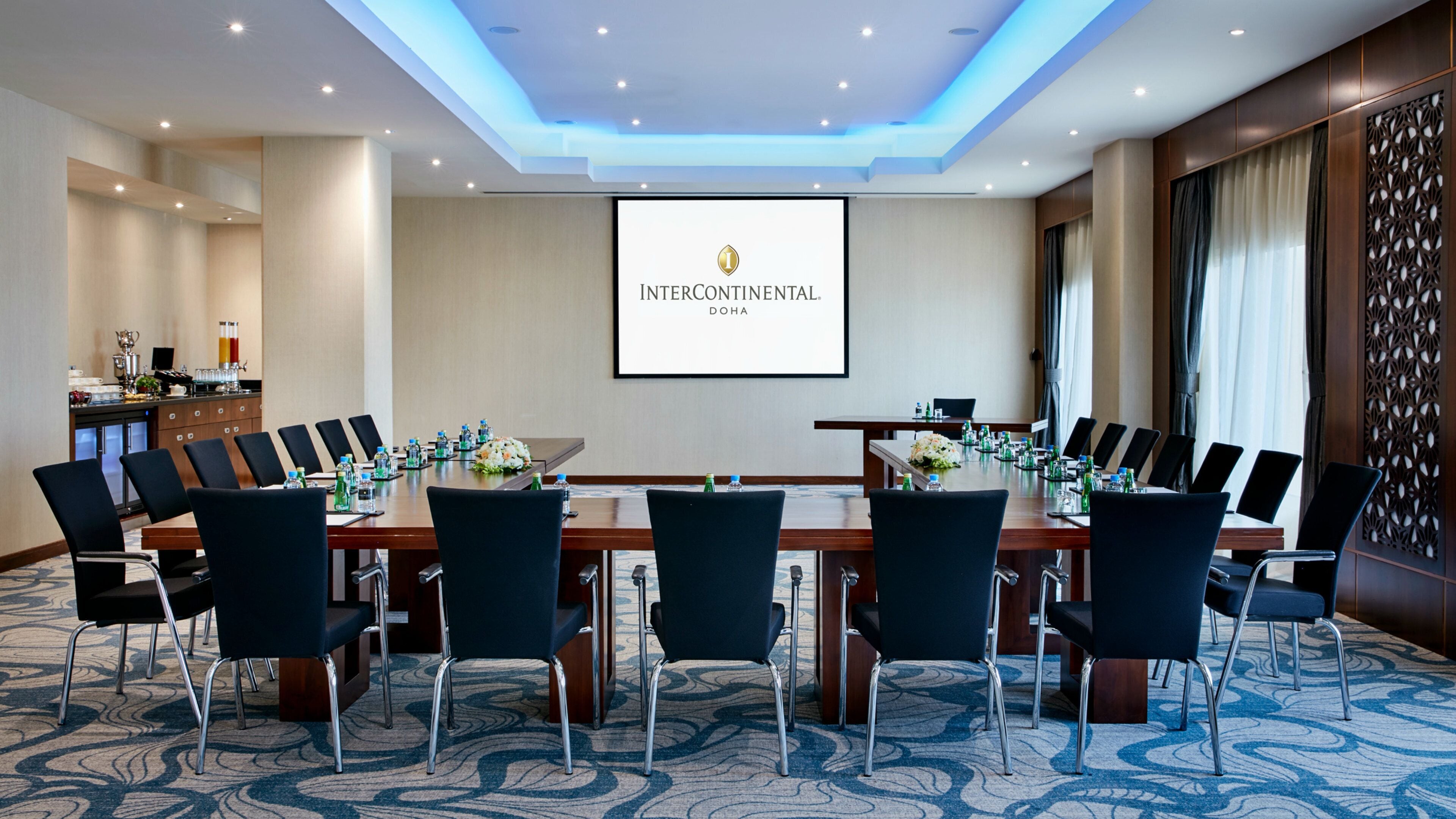 Ein Konferenzraum mit einem langen Tisch, Stühlen und einem Bildschirm, der 'INTERCONTINENTAL DOHA' anzeigt.