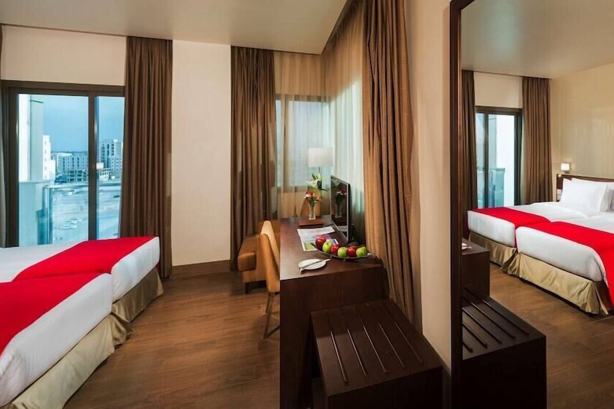 Hotelkamer met twee bedden, een bureau, een stoel en een groot raam met uitzicht op de stad.
