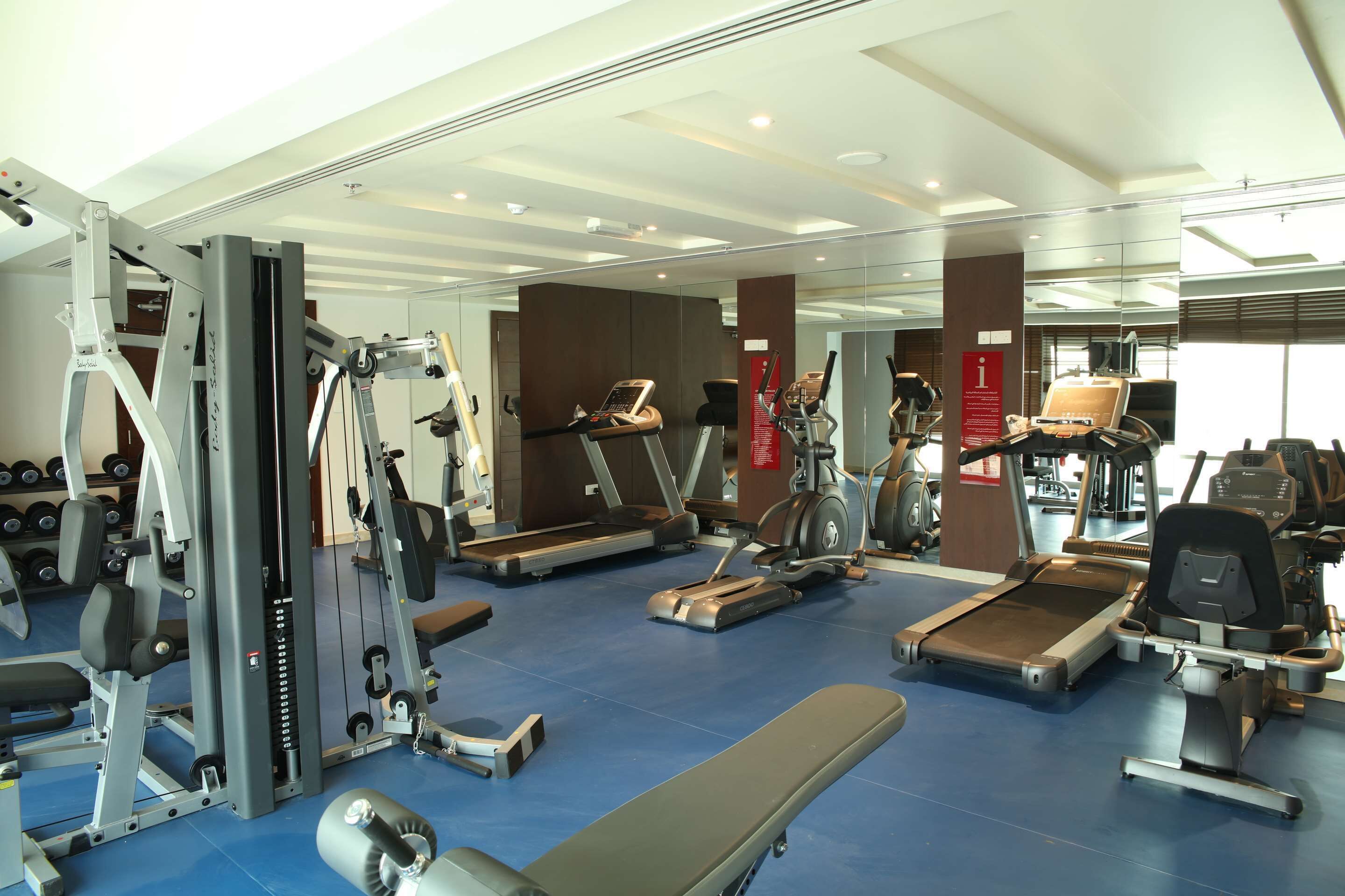 Une salle de sport équipée de divers appareils d’exercice, notamment des tapis de course, des appareils de musculation et des haltères.