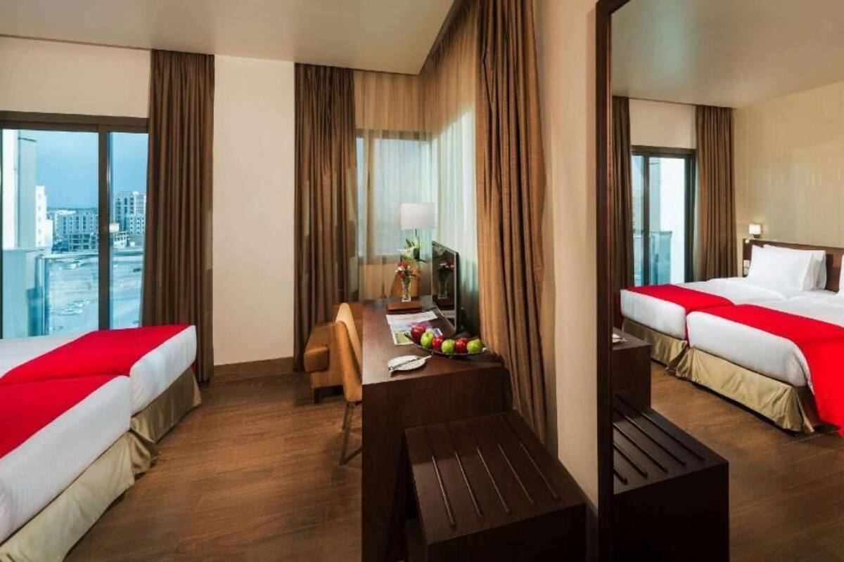 Een hotelkamer met twee bedden, een eettafel, een stoel, een lamp en uitzicht op de stad.