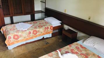 A hotel room with two beds, wooden headboards, a small bedside table with a remote control, and a wooden floor.