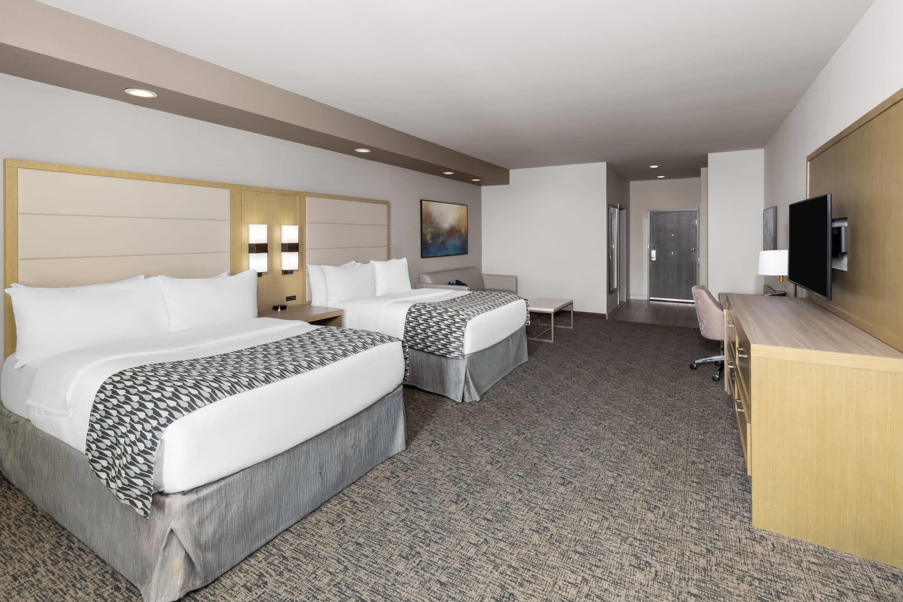 A hotel room with two beds, a desk, a TV, and a painting on the wall.