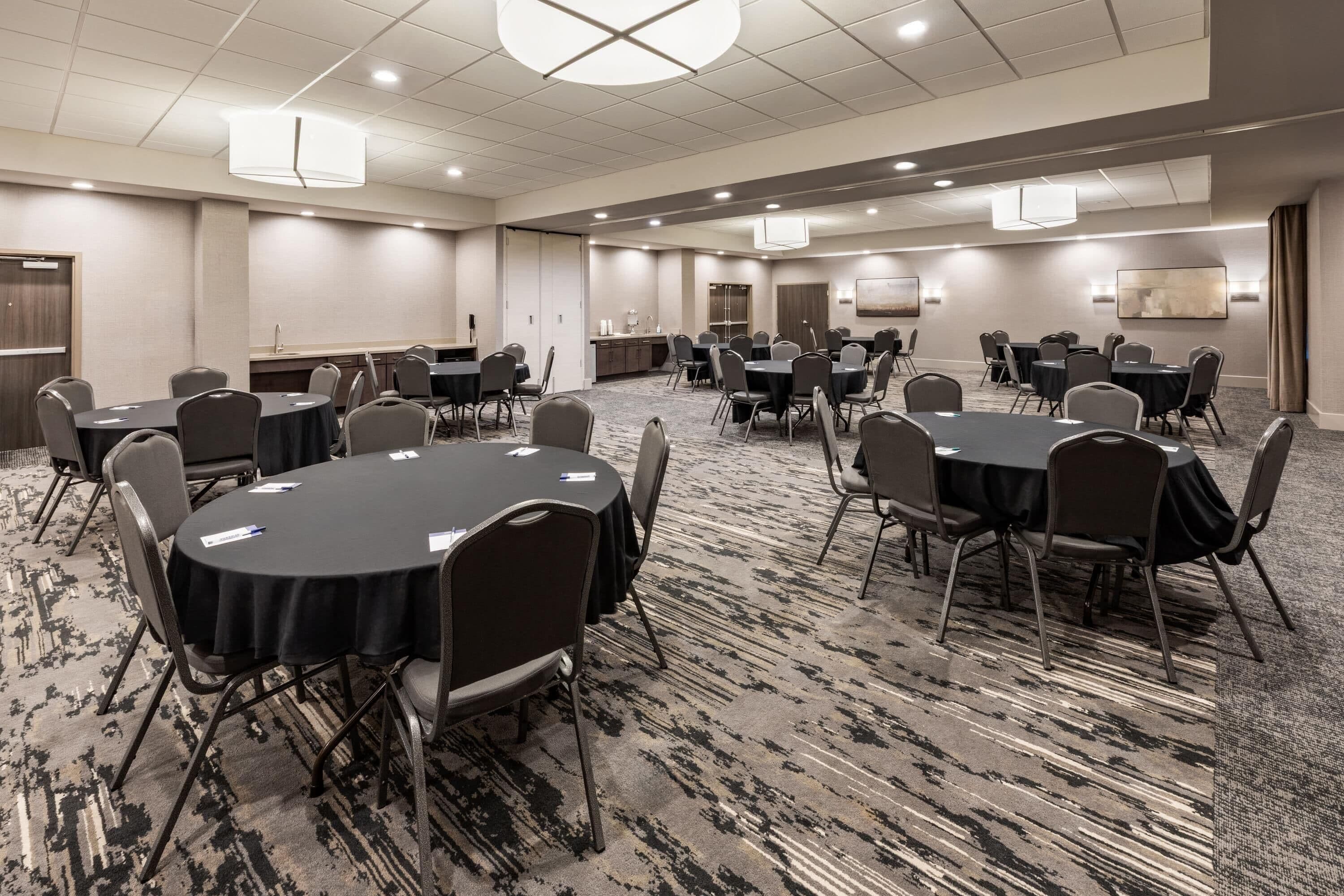 A conference room with multiple tables and chairs, carpeted flooring, and recessed lighting.