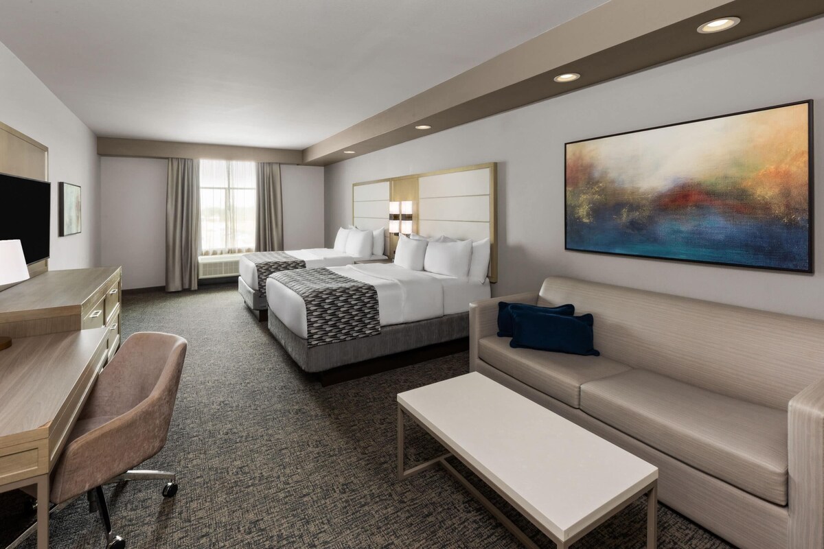 A hotel room with two beds, a desk, a chair, a sofa, and a large abstract painting on the wall.