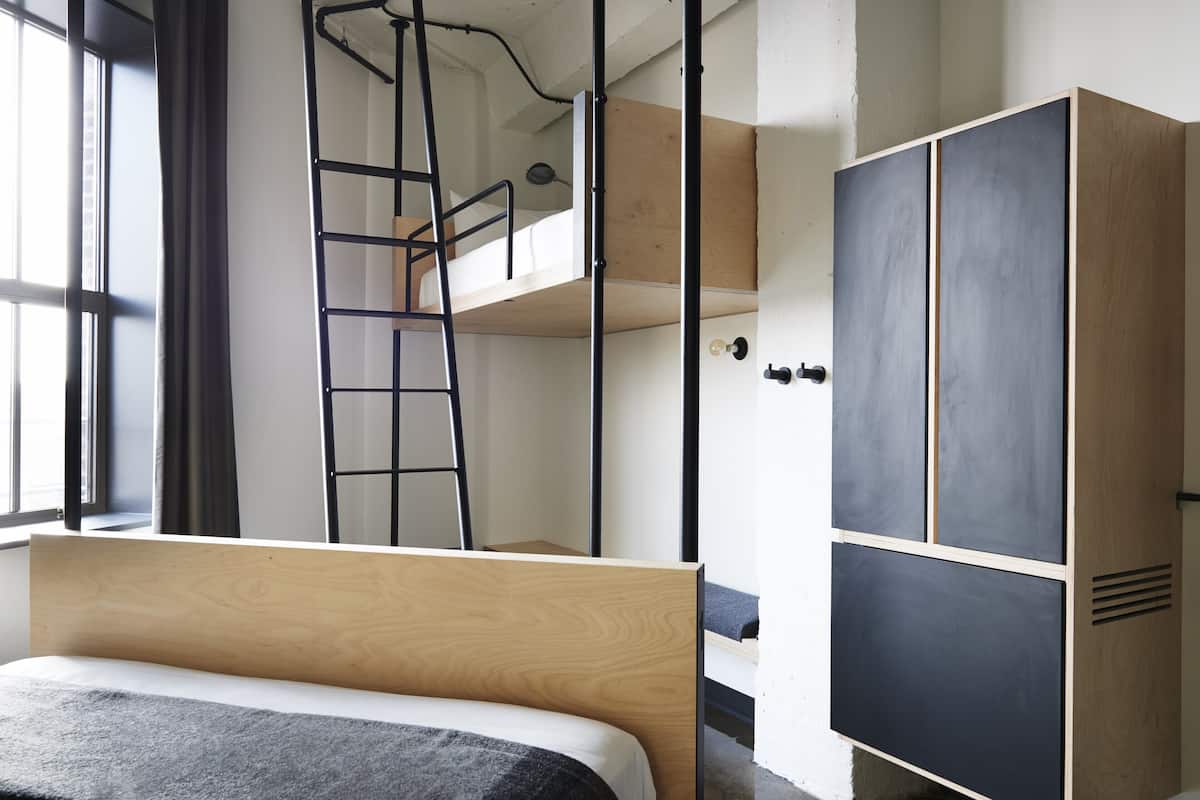 A bunk bed with a ladder, a wardrobe, and a window with curtains.