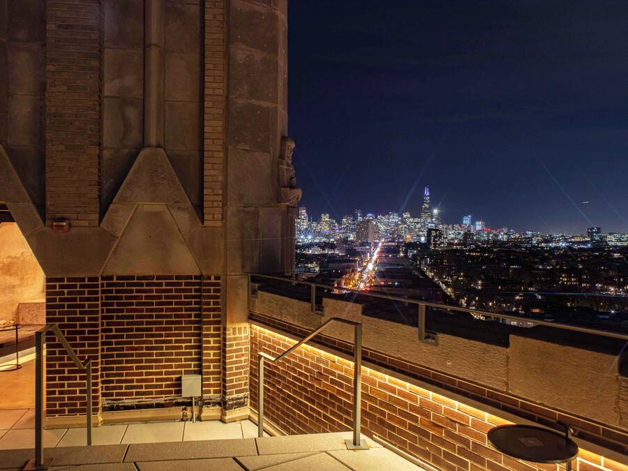 A nighttime view from a high vantage point overlooking a cityscape with illuminated buildings and a river.