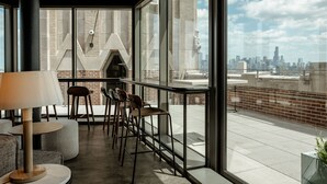 A modern interior with a bar area, seating, and large windows offering a city view.