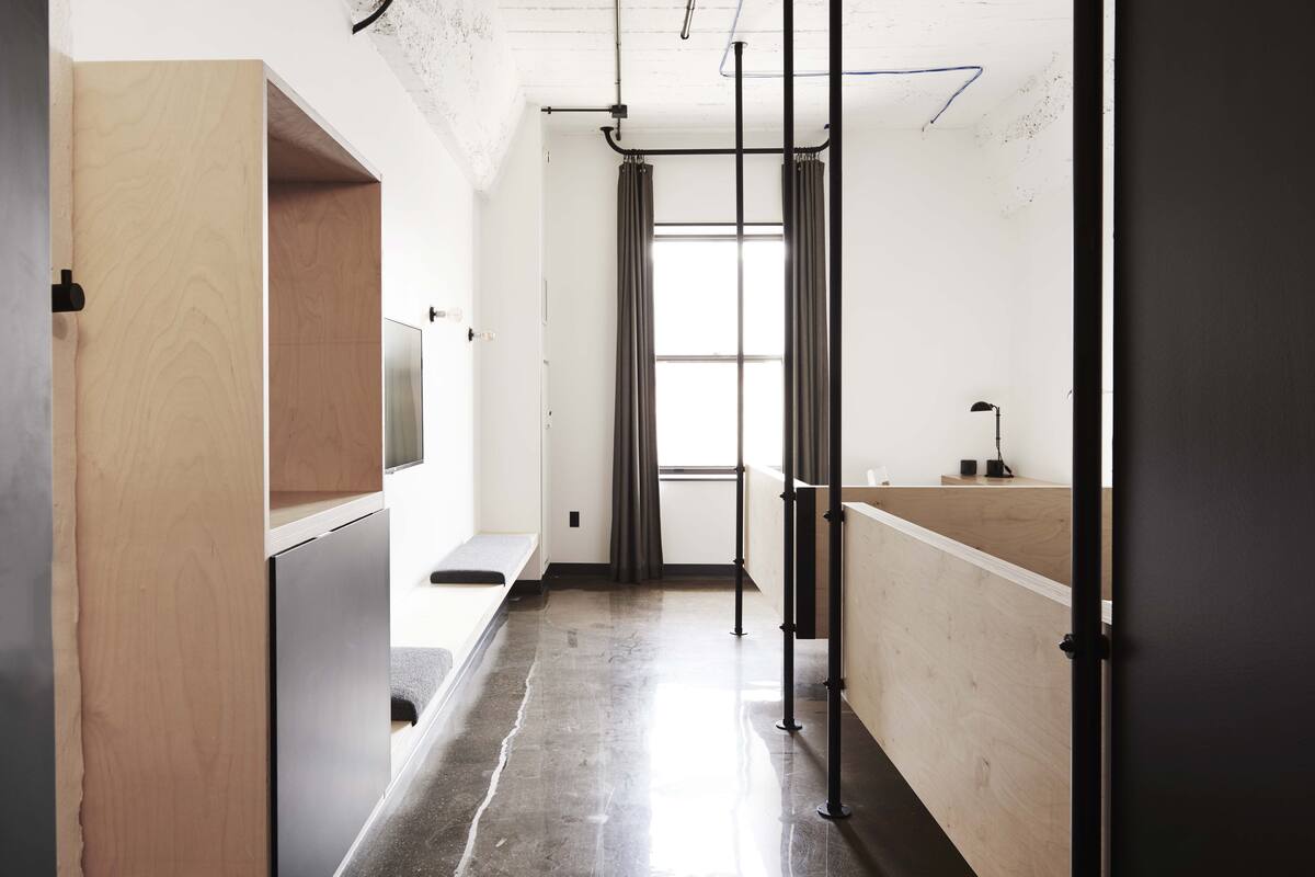 A modern, minimalist bathroom with a wooden vanity, a bench, and a large window with curtains.