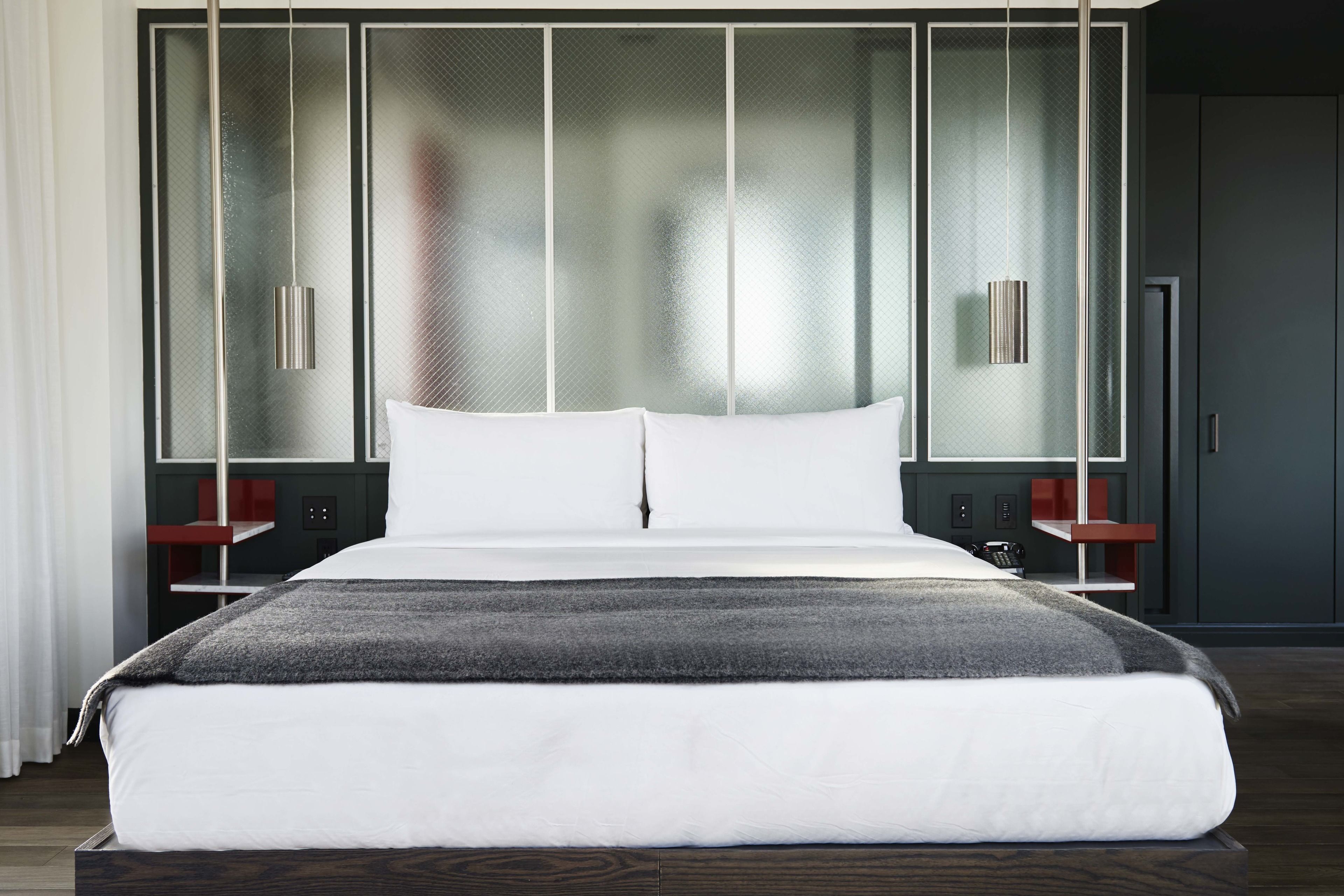 Una habitación de hotel moderna con una cama grande, un separador de vidrio y un diseño minimalista.