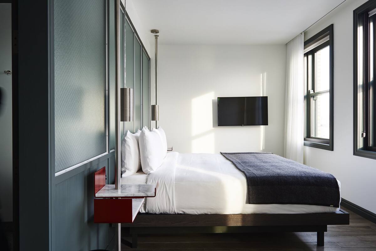 A modern bedroom with a bed, a TV mounted on the wall, and large windows.