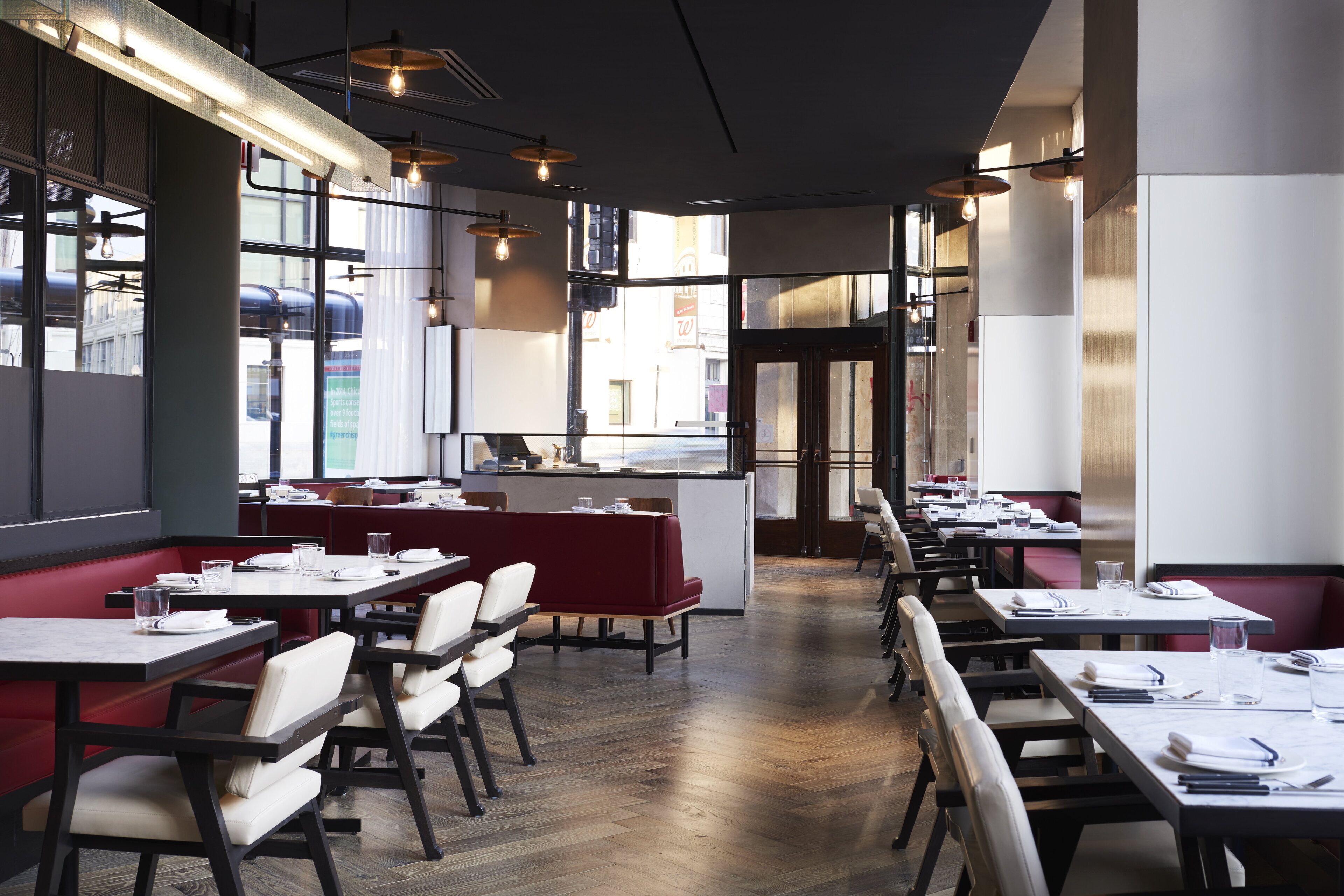 A modern restaurant interior with high tables and booths, large windows, and pendant lighting.