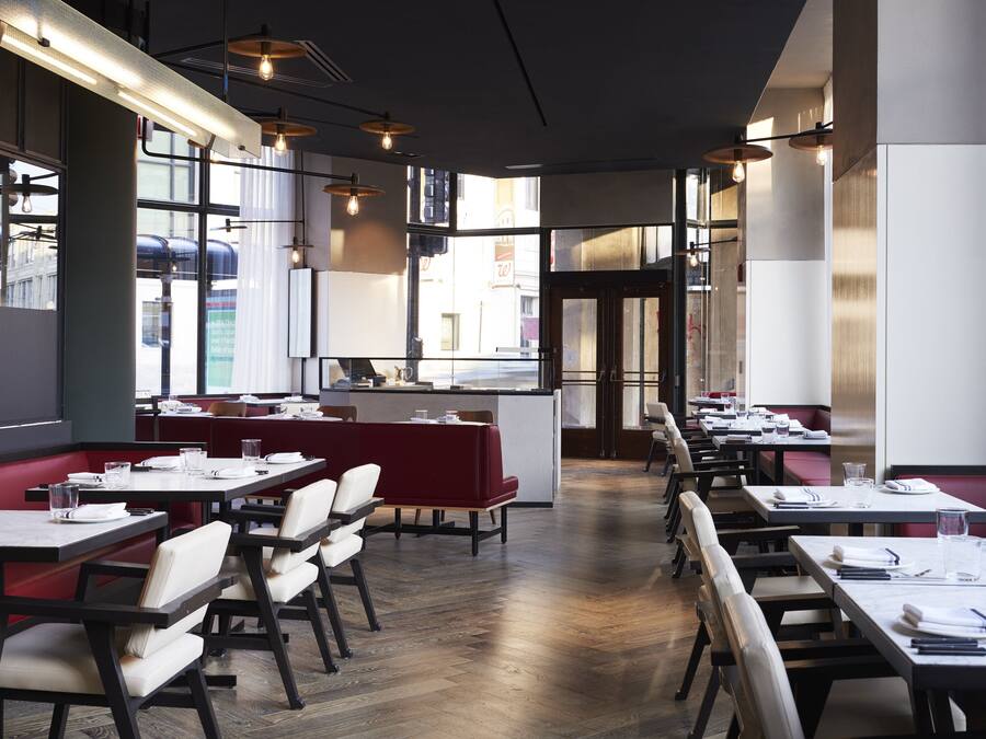 A modern restaurant interior with high tables and booths, large windows, and pendant lighting.