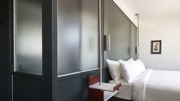 A modern hotel room with a bed, a small bedside table, a nightstand, and a wall-mounted lamp.