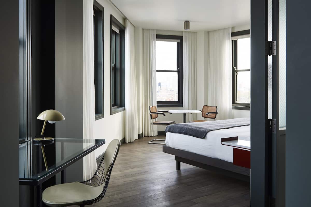A modern hotel room with a bed, a desk, and two chairs.