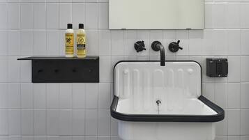 Een badkamer met een witte wasbak, een zwarte kraan en twee flessen shampoo op een zwart schap.