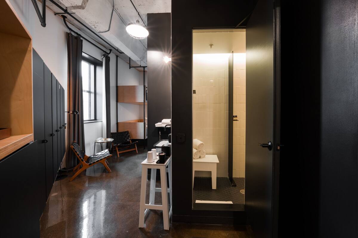 A modern bathroom with a glass door, a shower, and a toilet. There is a small seating area with a chair and a table.
