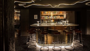 A bar area with a circular bar, stools, and a well-stocked shelf of bottles.