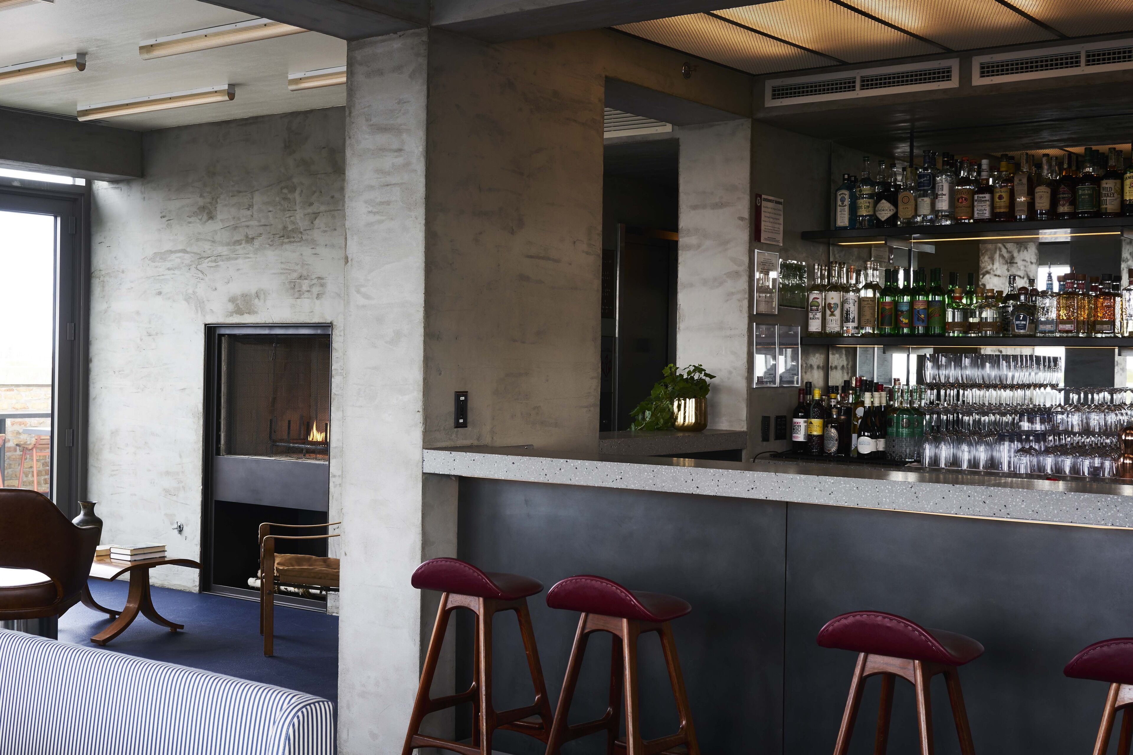 A bar area with stools, a fireplace, and a bar stocked with bottles and glasses.