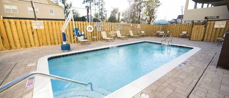 A rectangular pool with a wooden fence, lounge chairs, and a lifeguard stand.