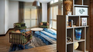 Een moderne woonkamer met een houten vloer, twee groene fauteuils, een ronde salontafel en een boekenplank met decoratieve objecten.