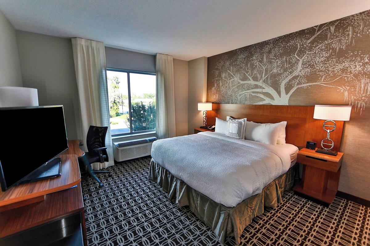 A hotel room with a large bed, a TV, a desk, and a window with curtains.
