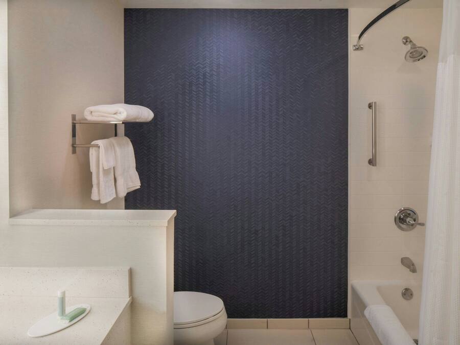 Un baño con inodoro, lavamanos con dispensador de jabón, toallero con toallas y zona de ducha con puerta de cristal.