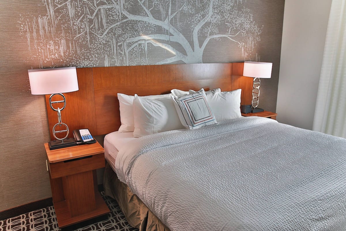 Una habitación de hotel con una cama grande, dos mesitas de noche con lámparas, un teléfono y un mural en la pared.
