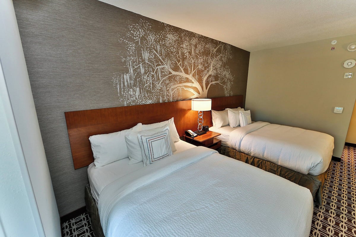Habitación de hotel con dos camas, una mesita de noche con lámpara y un mural en la pared.