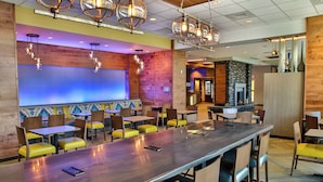 Een modern restaurant met een lange gedeelde tafel, gele stoelen met kussens en hangende吊灯.