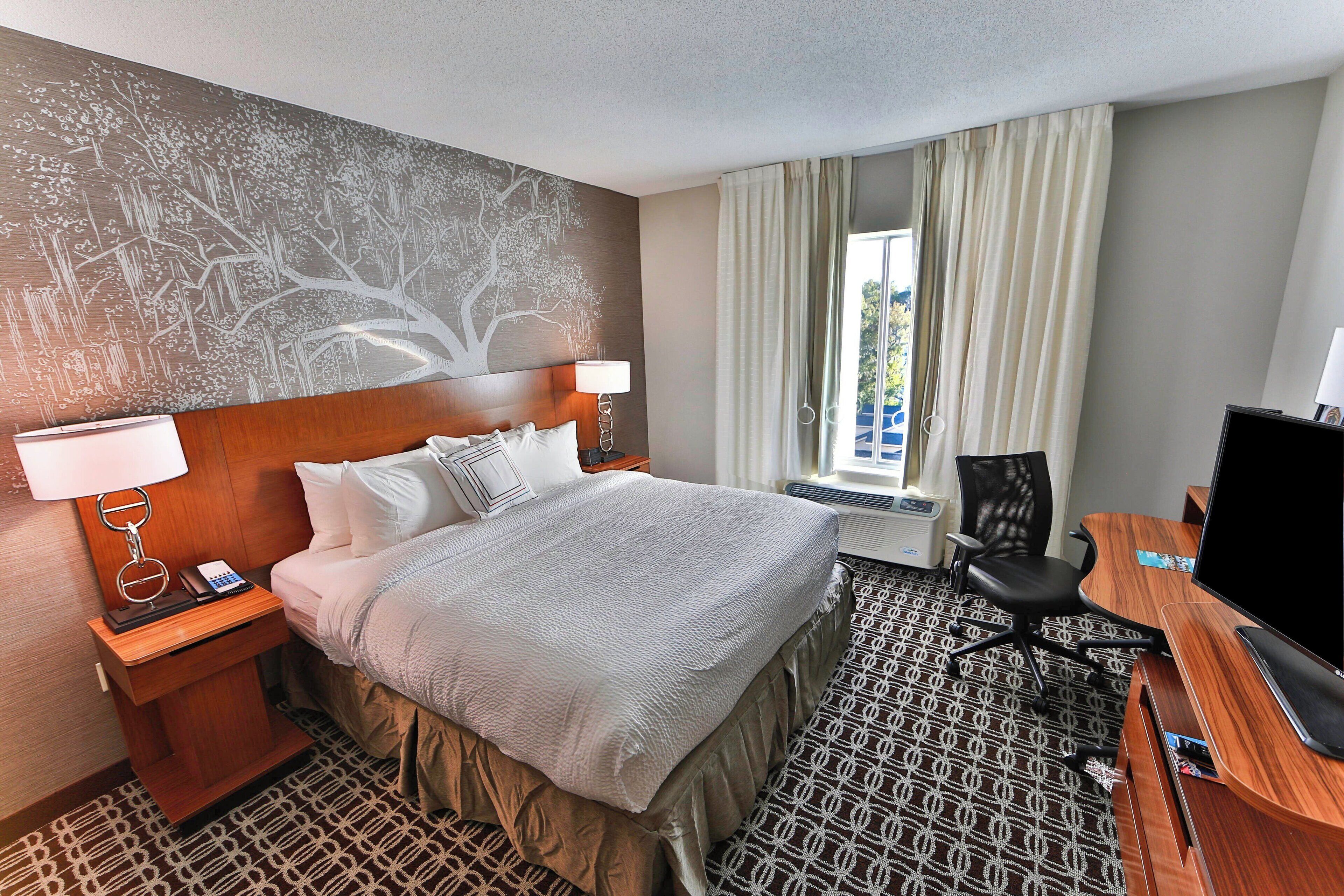 A hotel room with a large bed, a desk with a computer, a chair, a nightstand with a phone, and a wall mural.