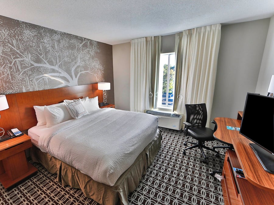 A hotel room with a large bed, a desk with a computer, a chair, a nightstand with a phone, and a wall mural.