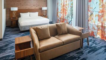 A hotel room with a bed, a sofa, a small table, and a nightstand.
