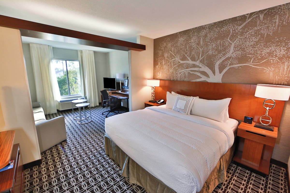 A hotel room with a large bed, a desk, a chair, a TV, and a painting on the wall.