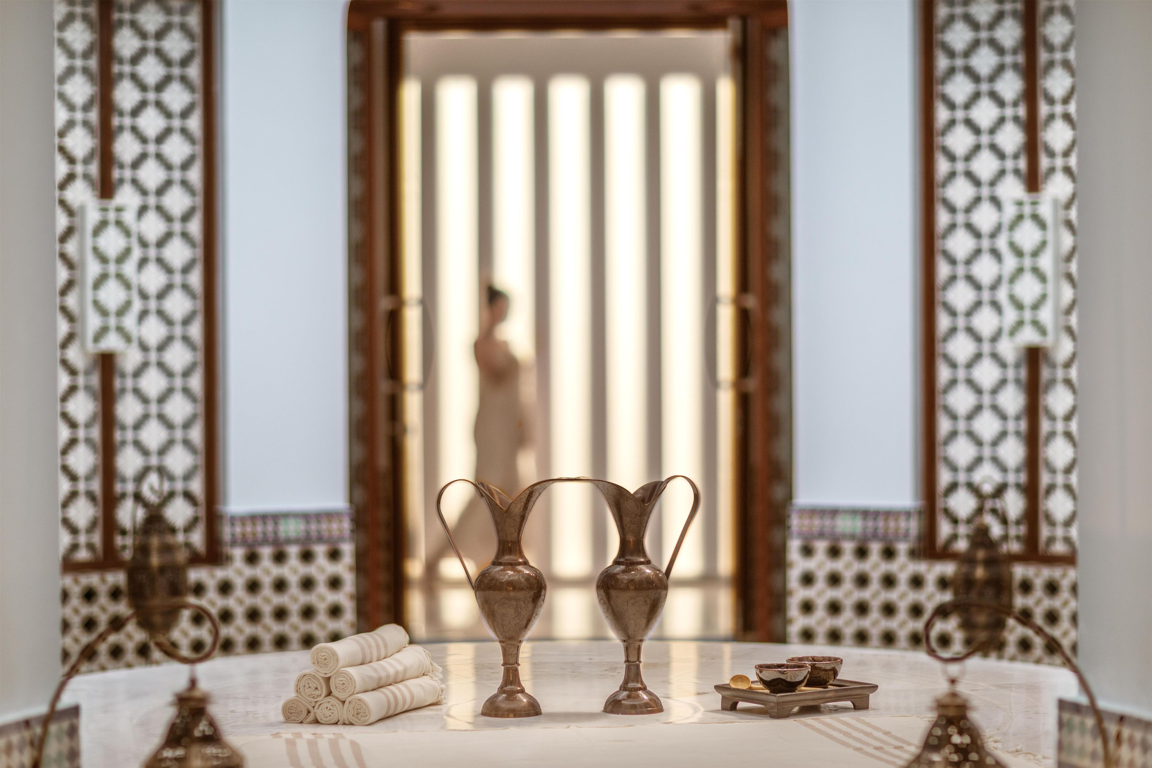 A room with a bed, two decorative vases, a small tray with bowls, and a patterned curtain.