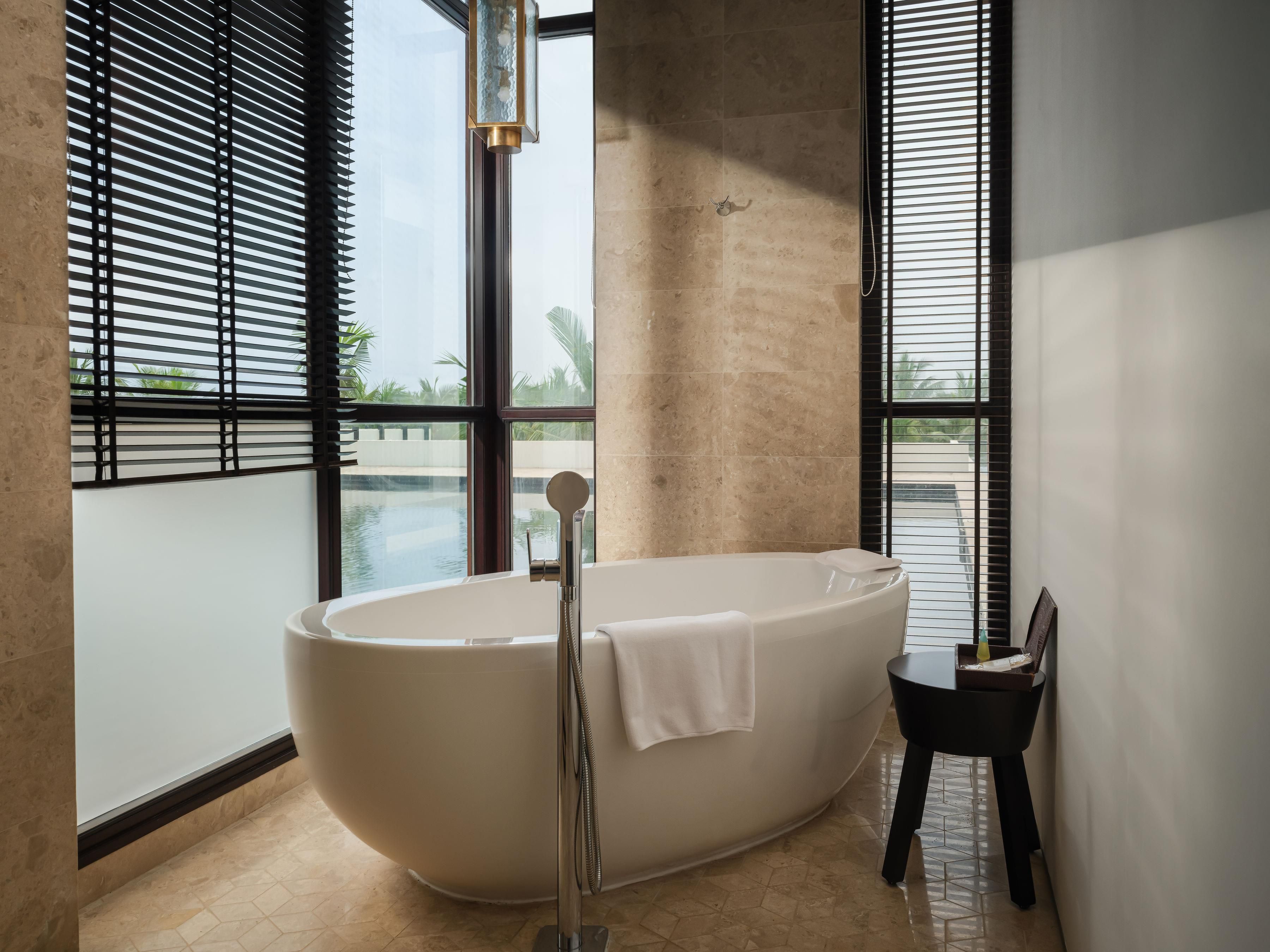 A modern bathroom with a freestanding bathtub, large windows, and a view of a pool.