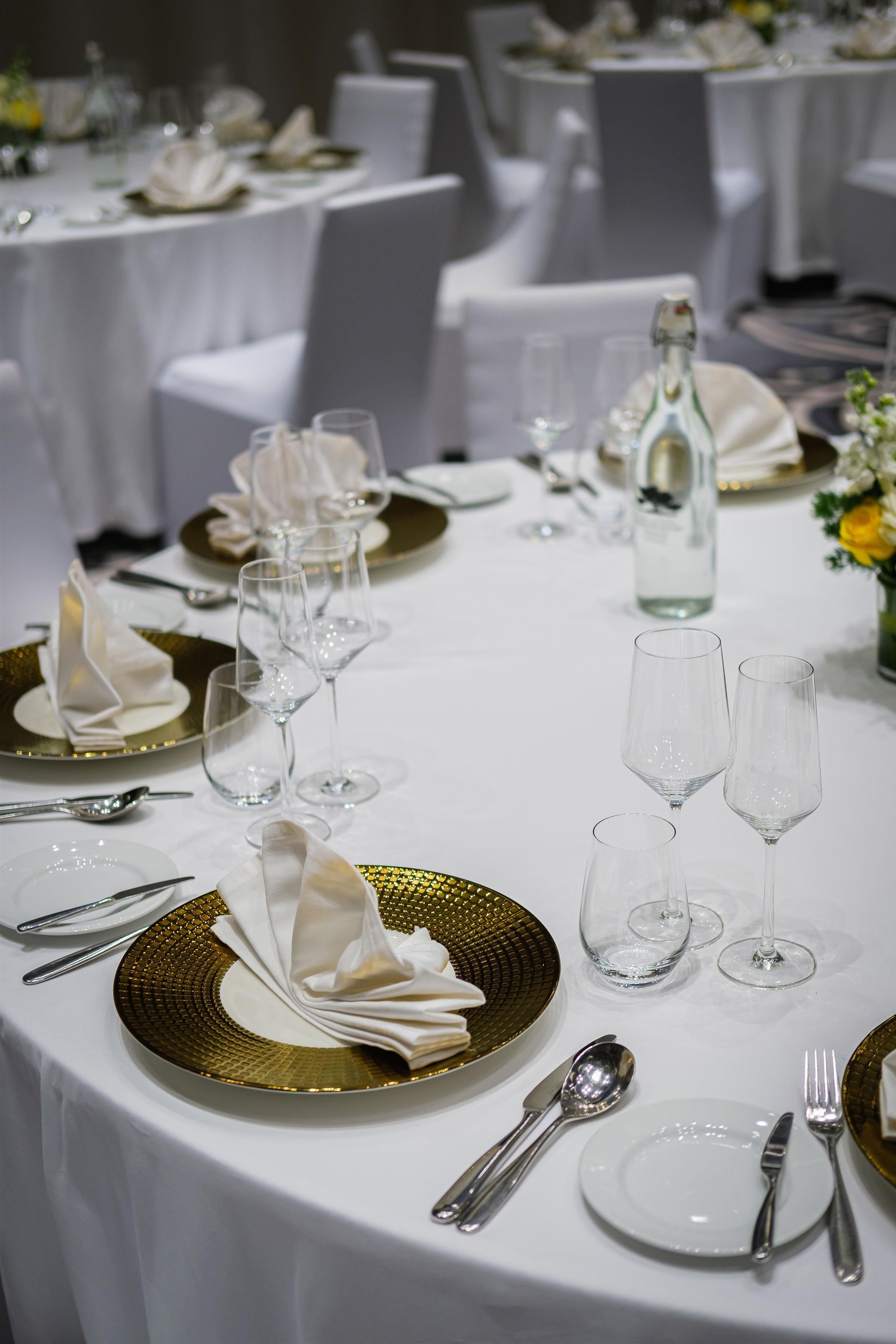 A table set for a formal dining experience with white tablecloths, gold-rimmed plates, and clear stemware.