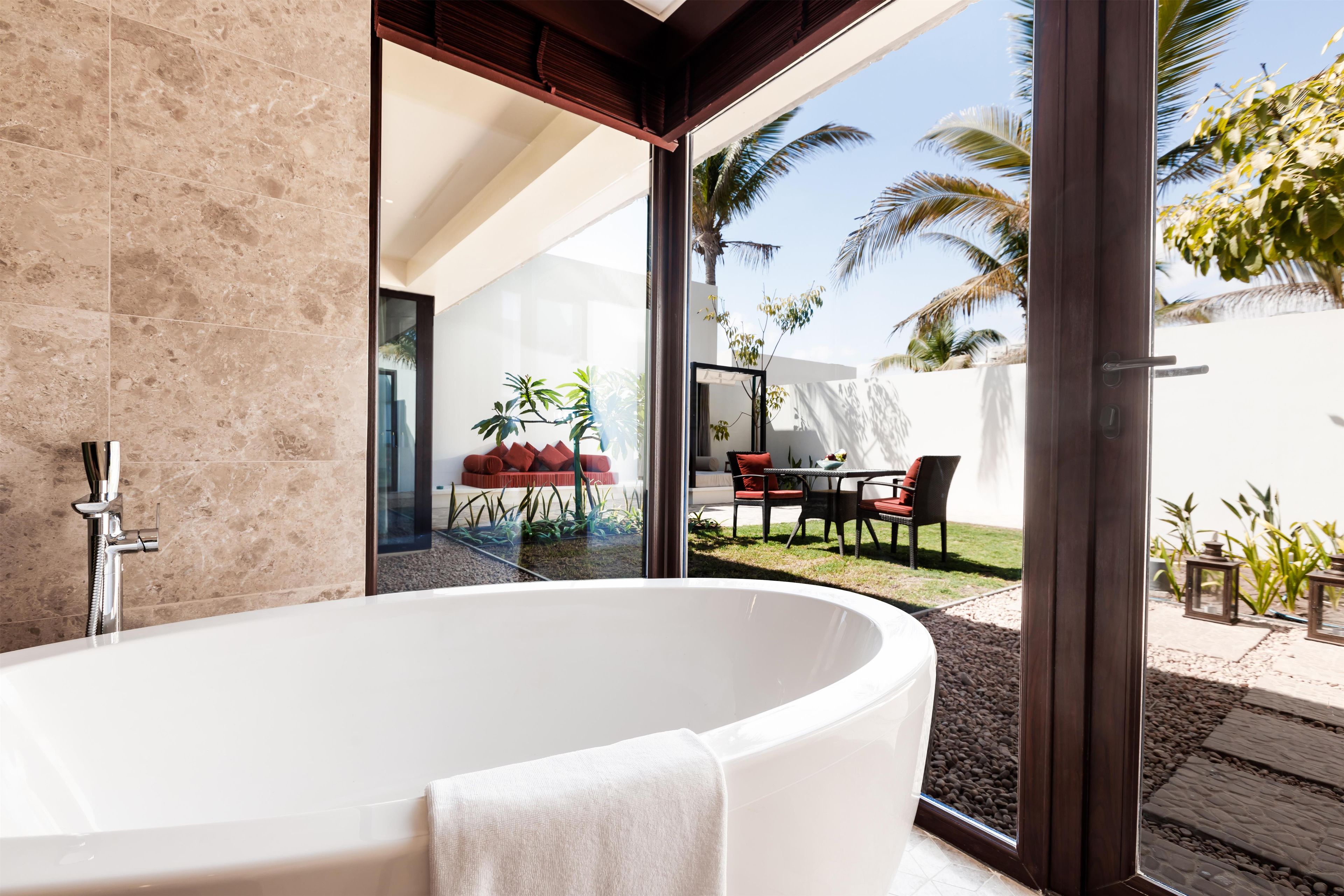 Ein modernes Badezimmer mit einer großzügigen, freistehenden Badewanne, einer Duschkabine aus Glas und Blick auf eine Außenpatio mit Möbeln und Pflanzen.