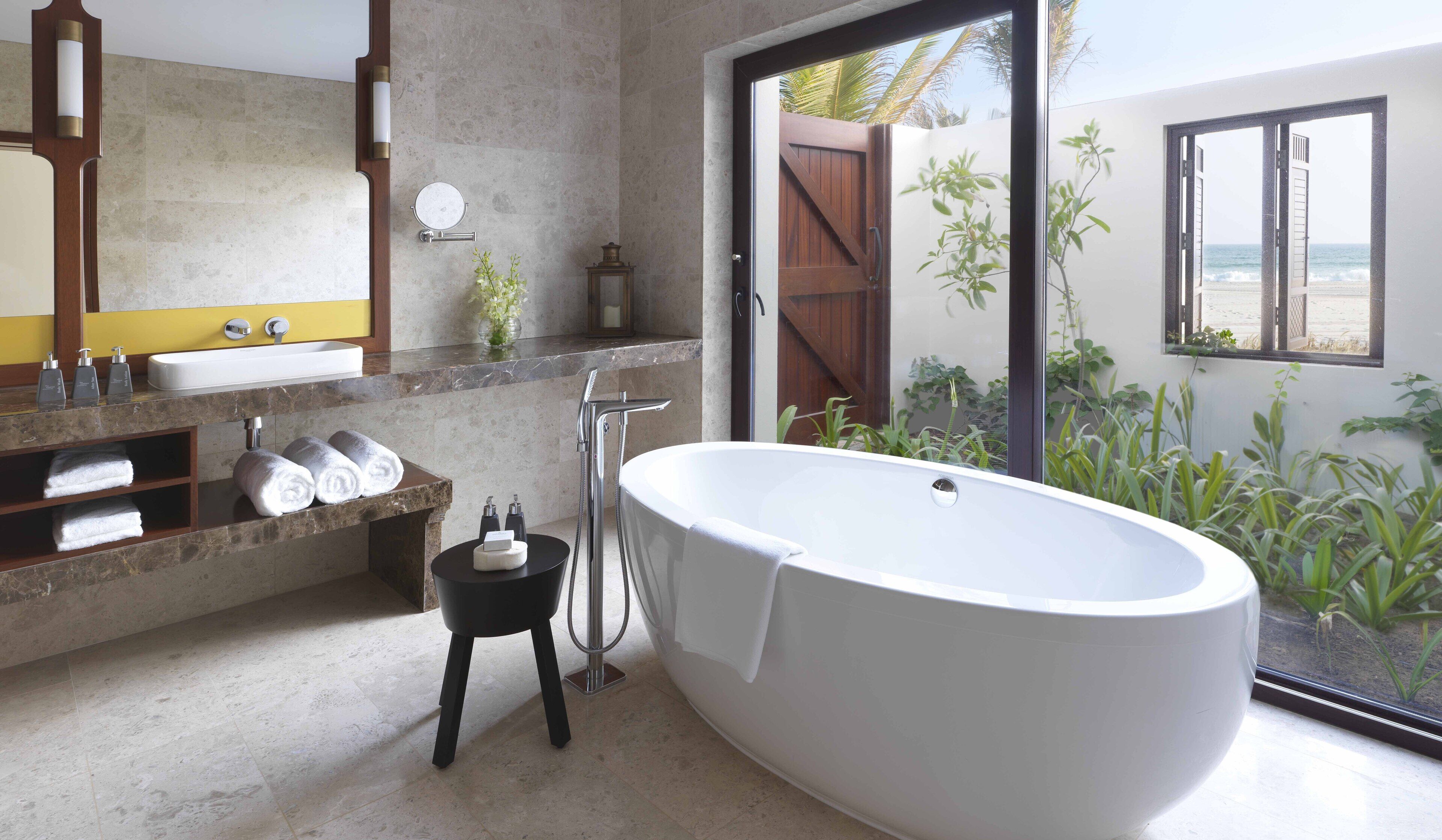Ein modernes Badezimmer mit einer freistehenden Badewanne, einem großen Spiegel und Meerblick.
