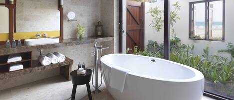 Ein modernes Badezimmer mit einer freistehenden Badewanne, einem großen Spiegel und Meerblick.