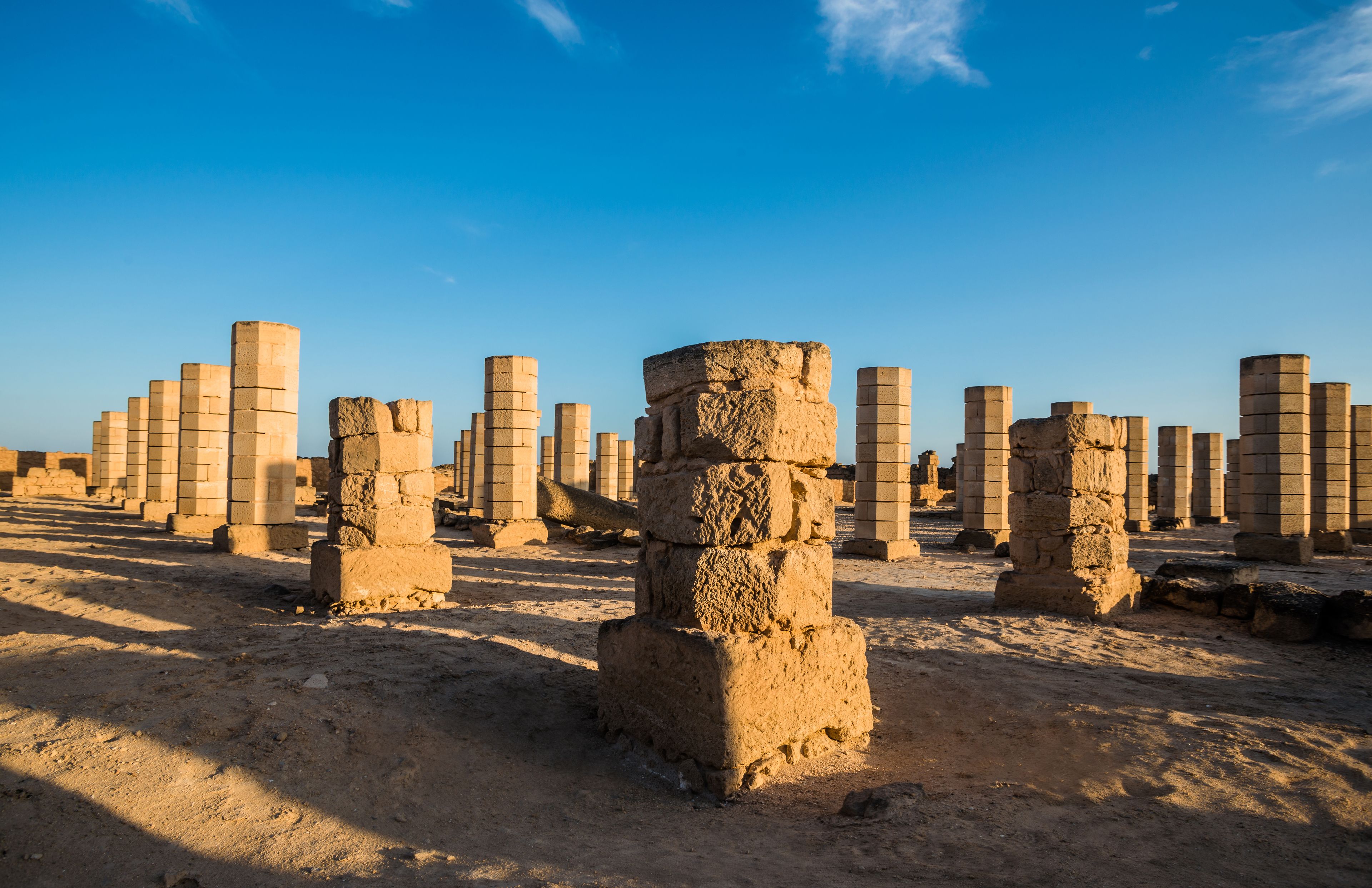 Antiche rovine in pietra con numerose colonne e un cielo azzurro intenso.