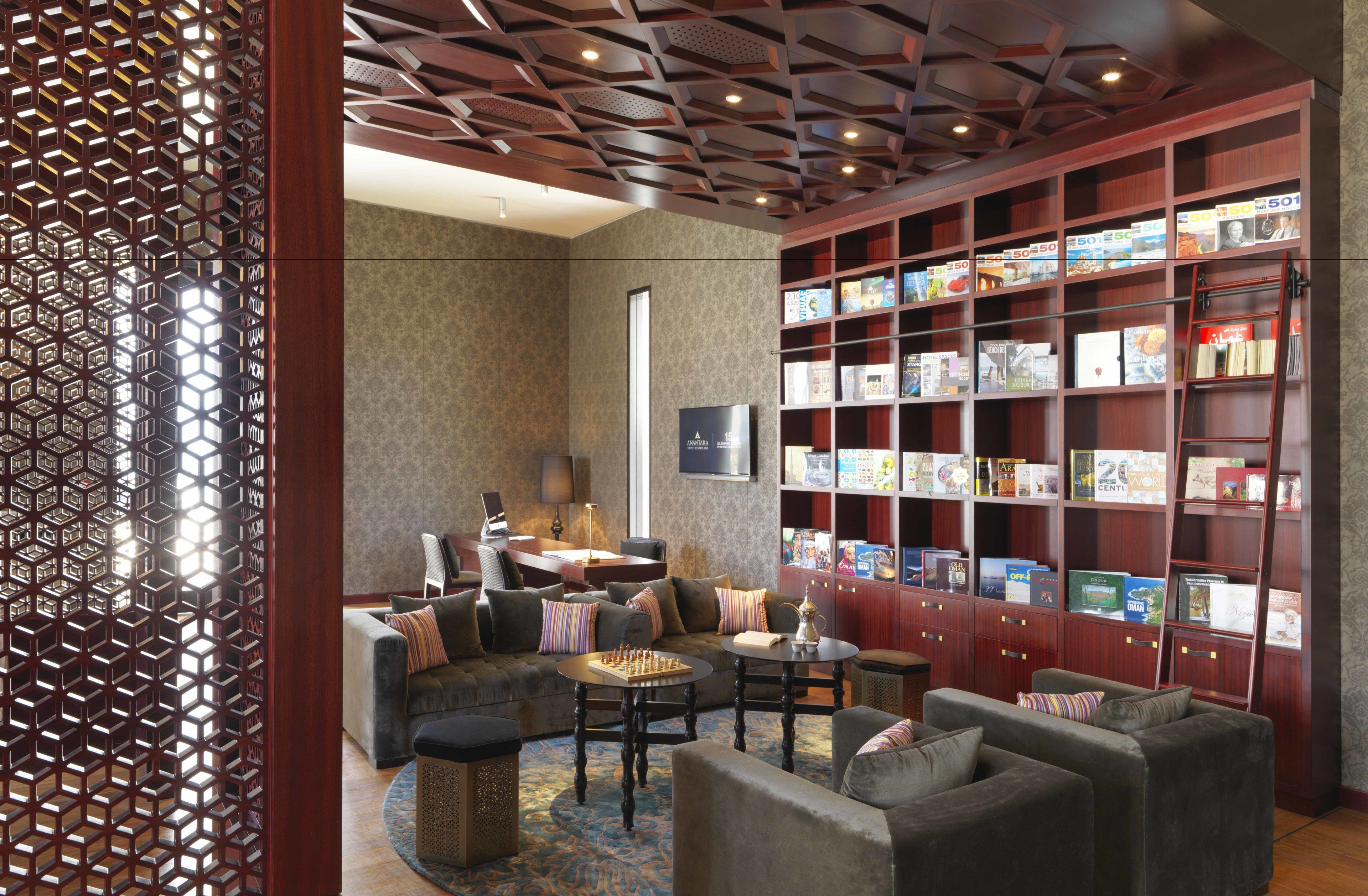 Eine moderne Lounge mit einer großen Bücherwand, bequemen Sitzgelegenheiten und einem dekorativen Holztrenner.
