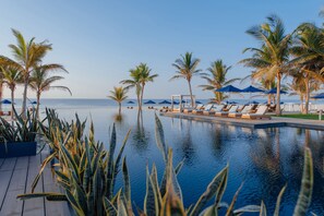 A poolside area with lounge chairs and palm trees, overlooking the ocean. - Al Baleed Resort Salalah by Anantara (Salalah)