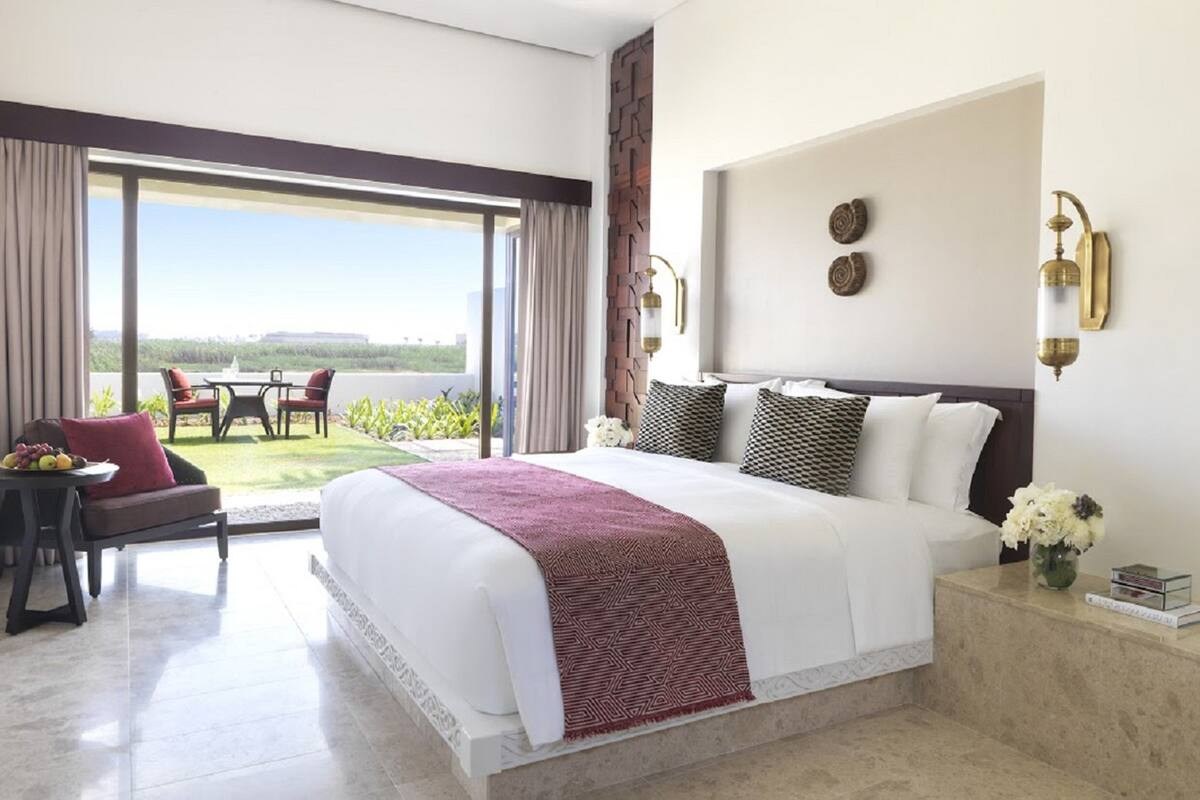 A hotel room with a large bed, a balcony with a table and chairs, and a view of the landscape.