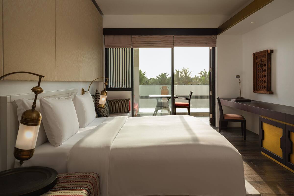 A hotel room with a large bed, a desk, and a balcony with a view.